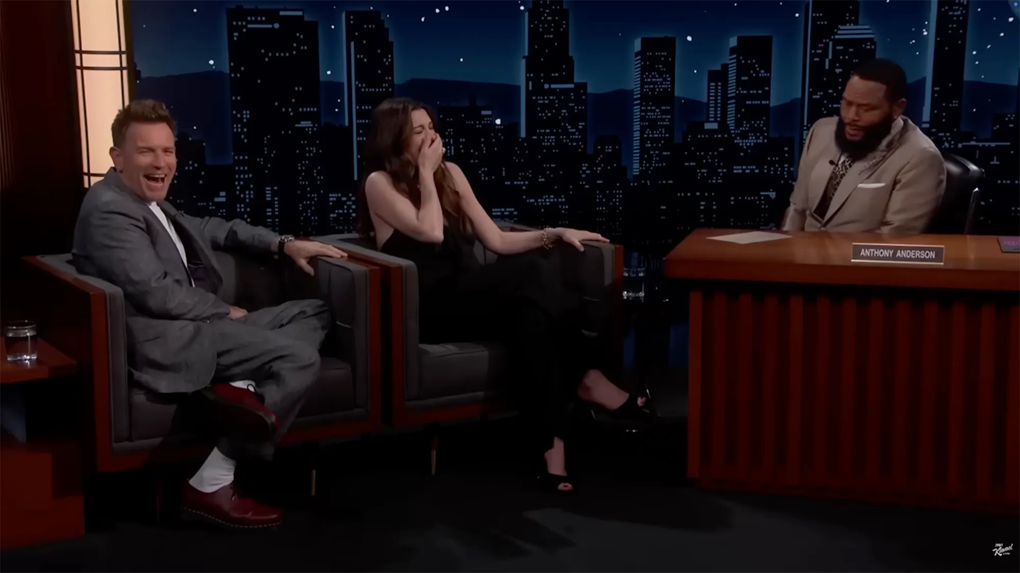 Actor Ewan McGregor and a female guest laugh on a late-night talk show set as host Anthony Anderson looks on.