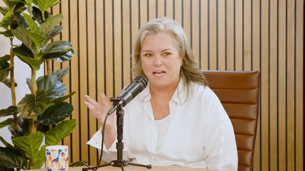 Rosie O'Donnell speaking into a microphone on a podcast.
