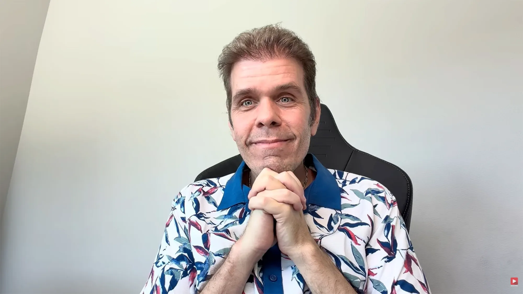 Perez Hilton smiling while wearing a tropical shirt and sitting in a gaming chair.