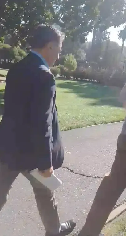 Xavier Becerra walking away from the camera, holding papers.