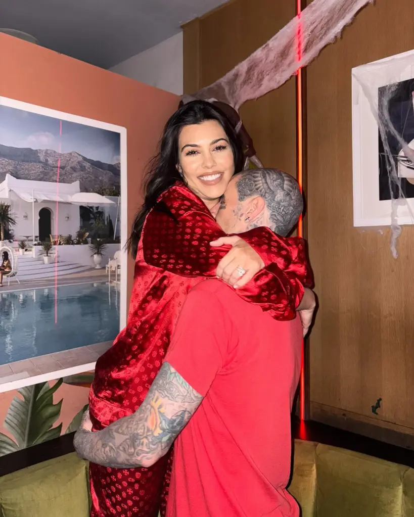 Kourtney Kardashian in red pajamas hugs Travis Barker, who is wearing a red shirt.